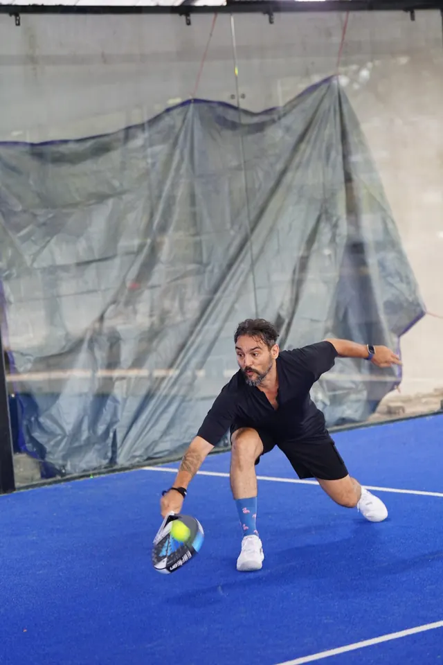 A padel player lunges low to return the ball.