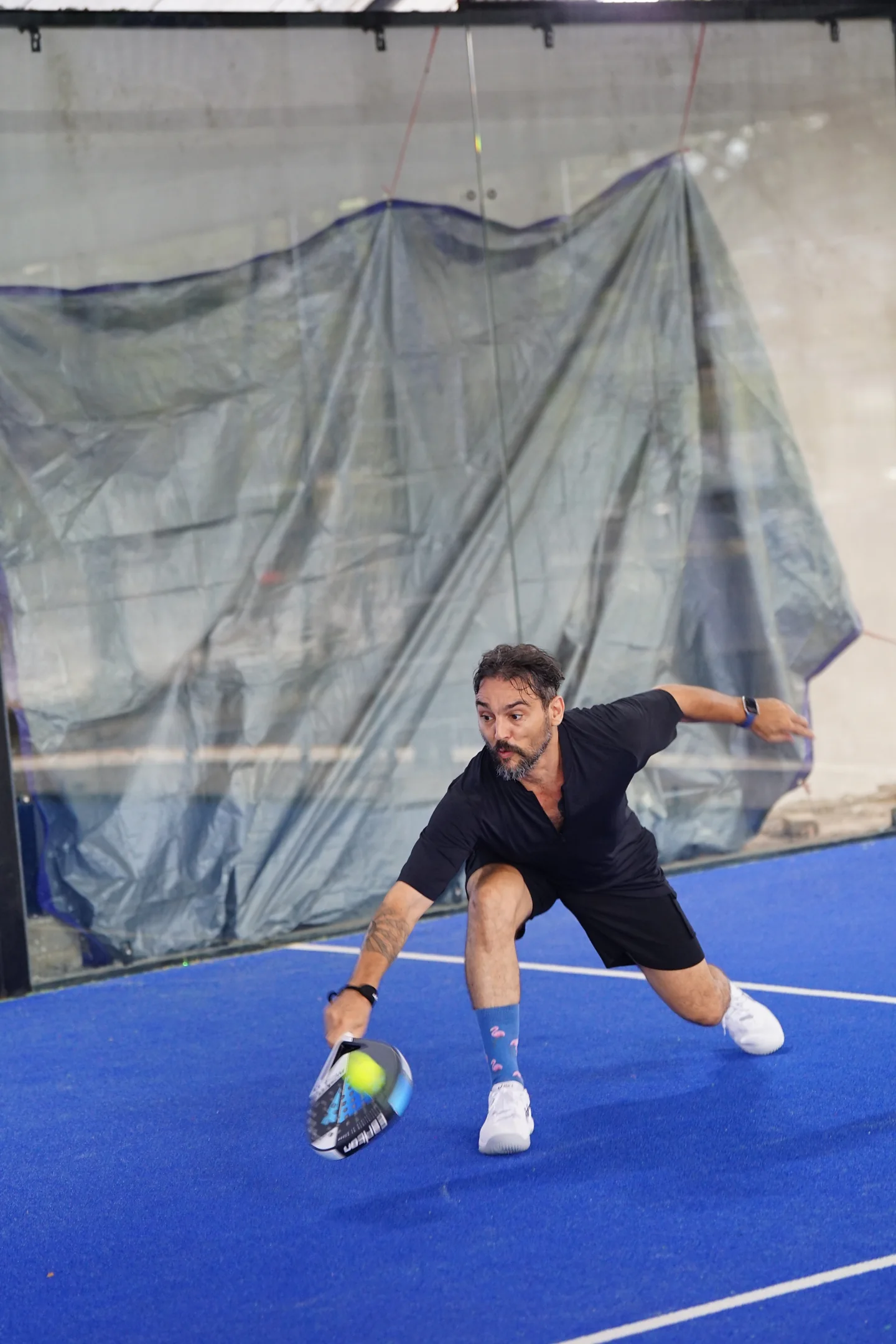 A padel player lunging to return a low ball on a blue court